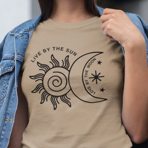 This t-shirt  design features a hand-drawn sketch of a sun & moon. The center of the sun is a spiral and there are fun flames stretching out from the sun. The moon overlaps part of the sun and is a crescent shape with three small stars next to it. Arced above the sun are the words "Live by the sun" and in the inside crescent of the moon it says "Love by the moon." This art is printed in black. 